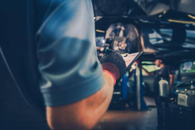 Technician wearing gloves writing on an inspection checklist during equipment maintenance in an industrial workshop.